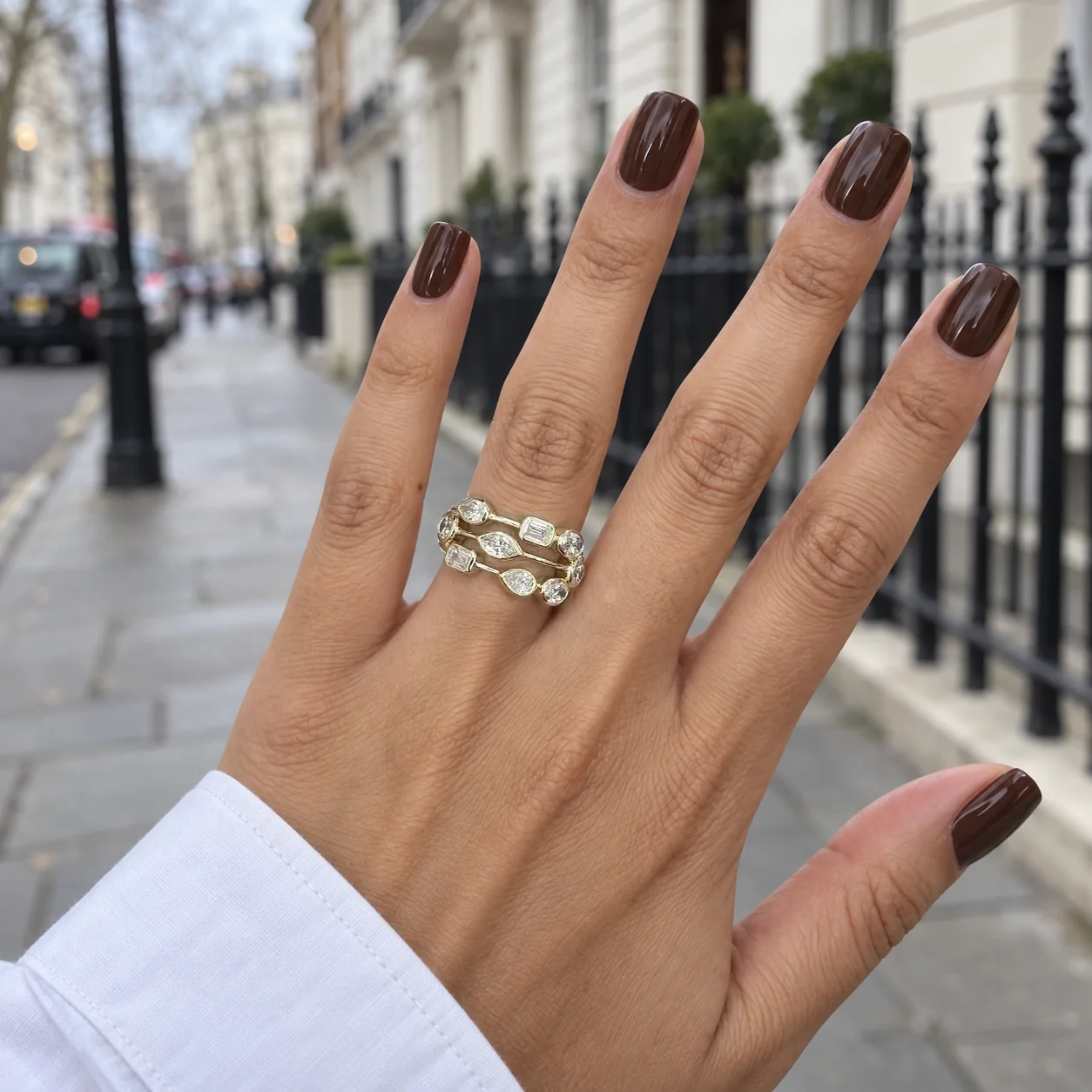 Mixed-shape gold diamond rings worn on a hand with a brown manicure on a London street