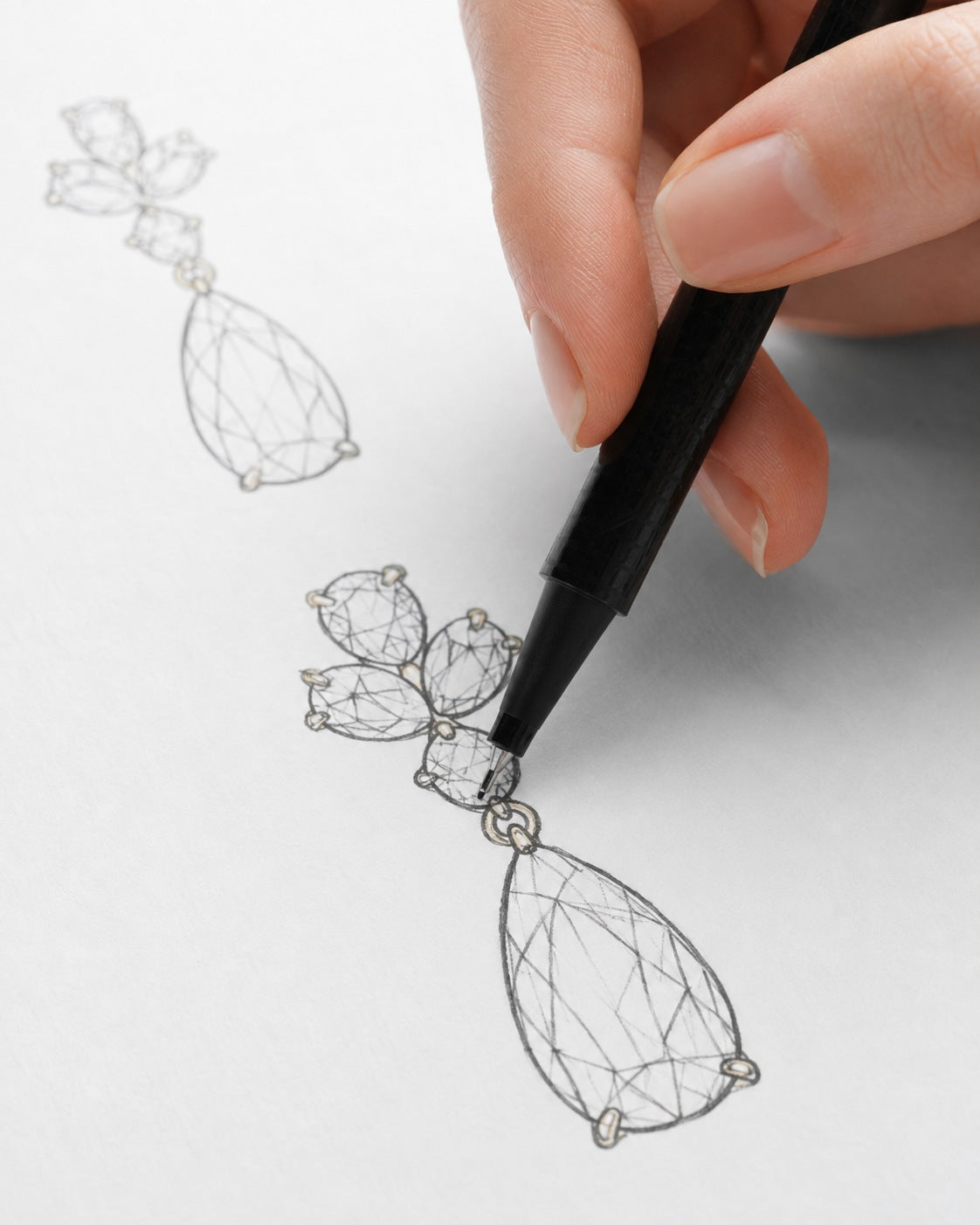 A jeweller sketching diamond cluster and pear-drop earrings by hand