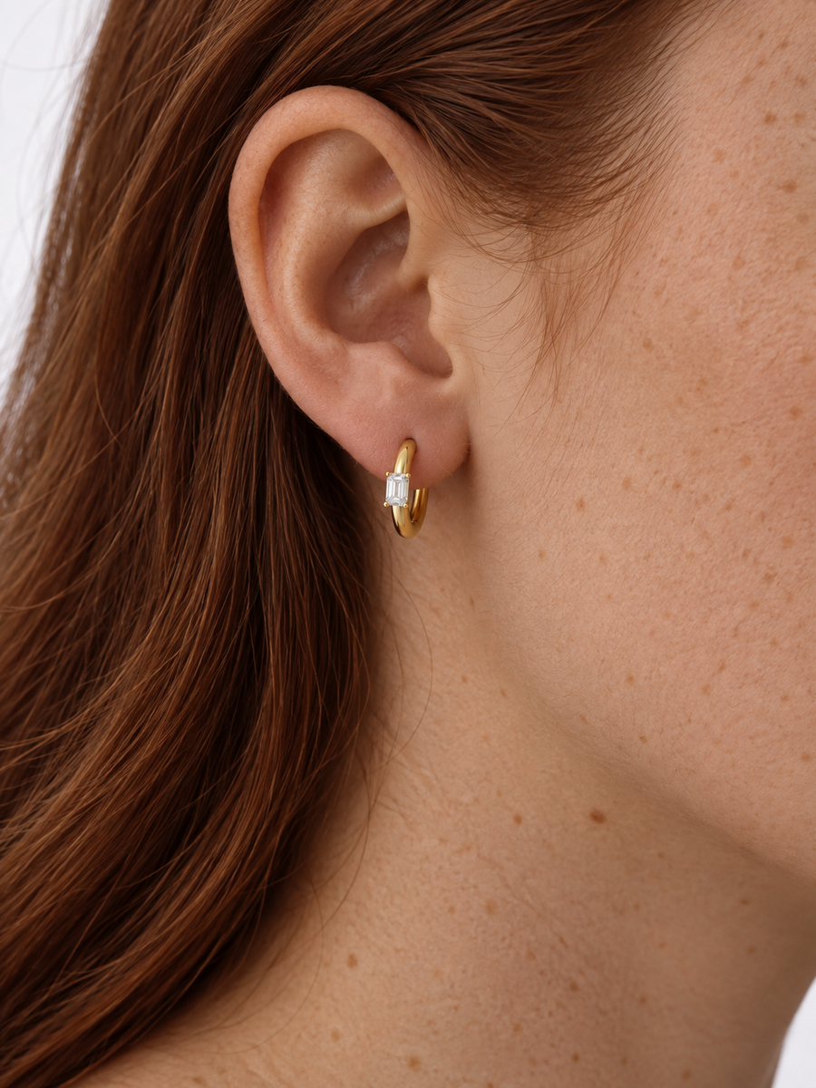 Emerald-cut natural diamond hoop earring in yellow gold worn on an ear