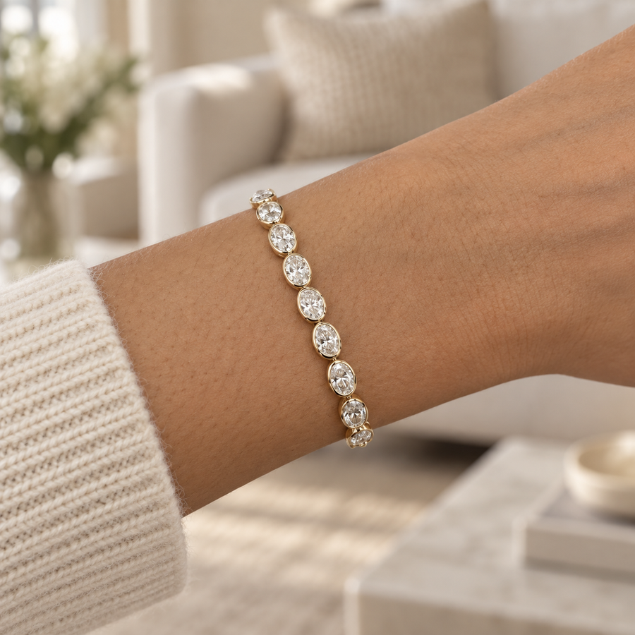 Oval bezel diamond tennis bracelet in yellow gold worn on a wrist