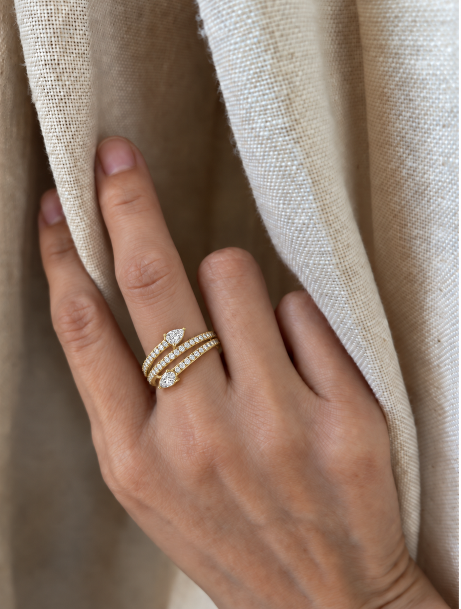 Oval and pear diamond wrap ring in yellow gold worn on a hand against linen