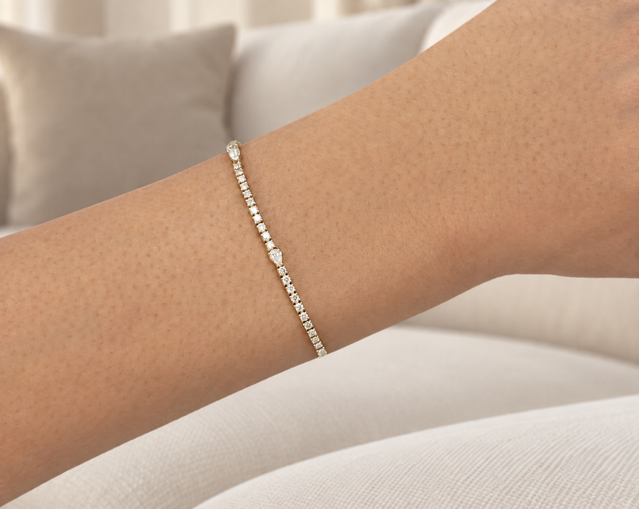 Pear and round natural diamond tennis bracelet in yellow gold worn on a wrist