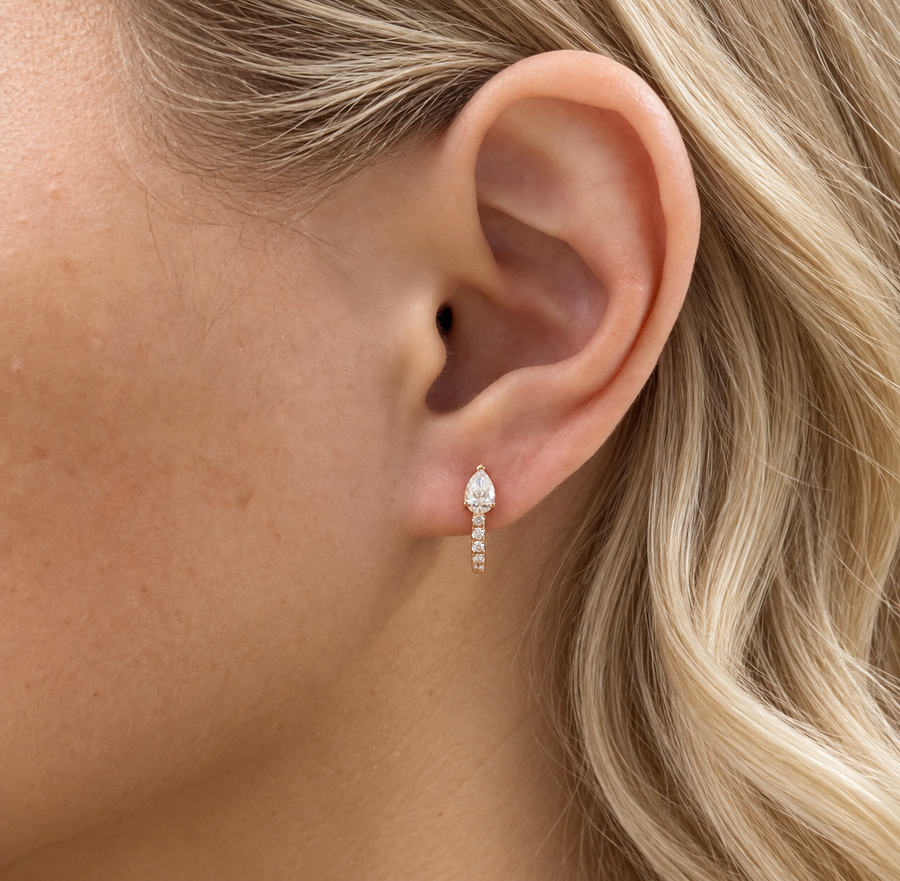 Pear diamond huggie earring in yellow gold worn on an ear