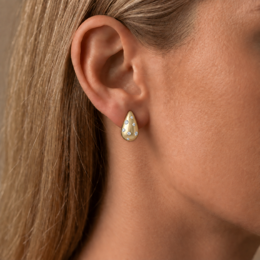 Scattered diamond teardrop earring in yellow gold worn on an ear