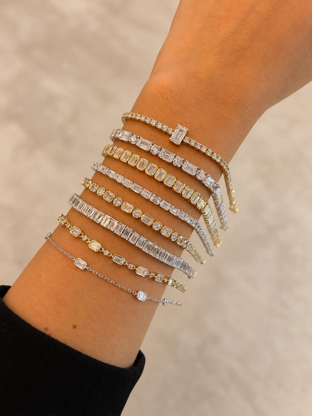 Diamond bracelets in yellow and white metals on a wrist against a neutral background