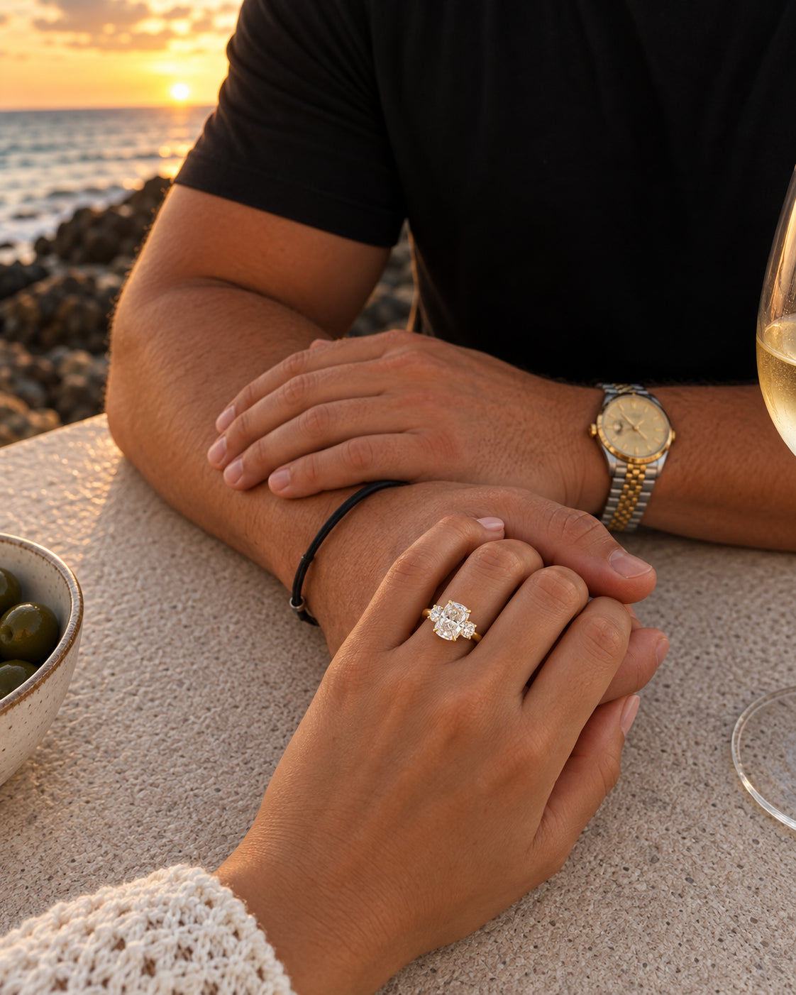 Illustrative concept: Yellow gold trilogy ring worn while holding hands at a seaside table