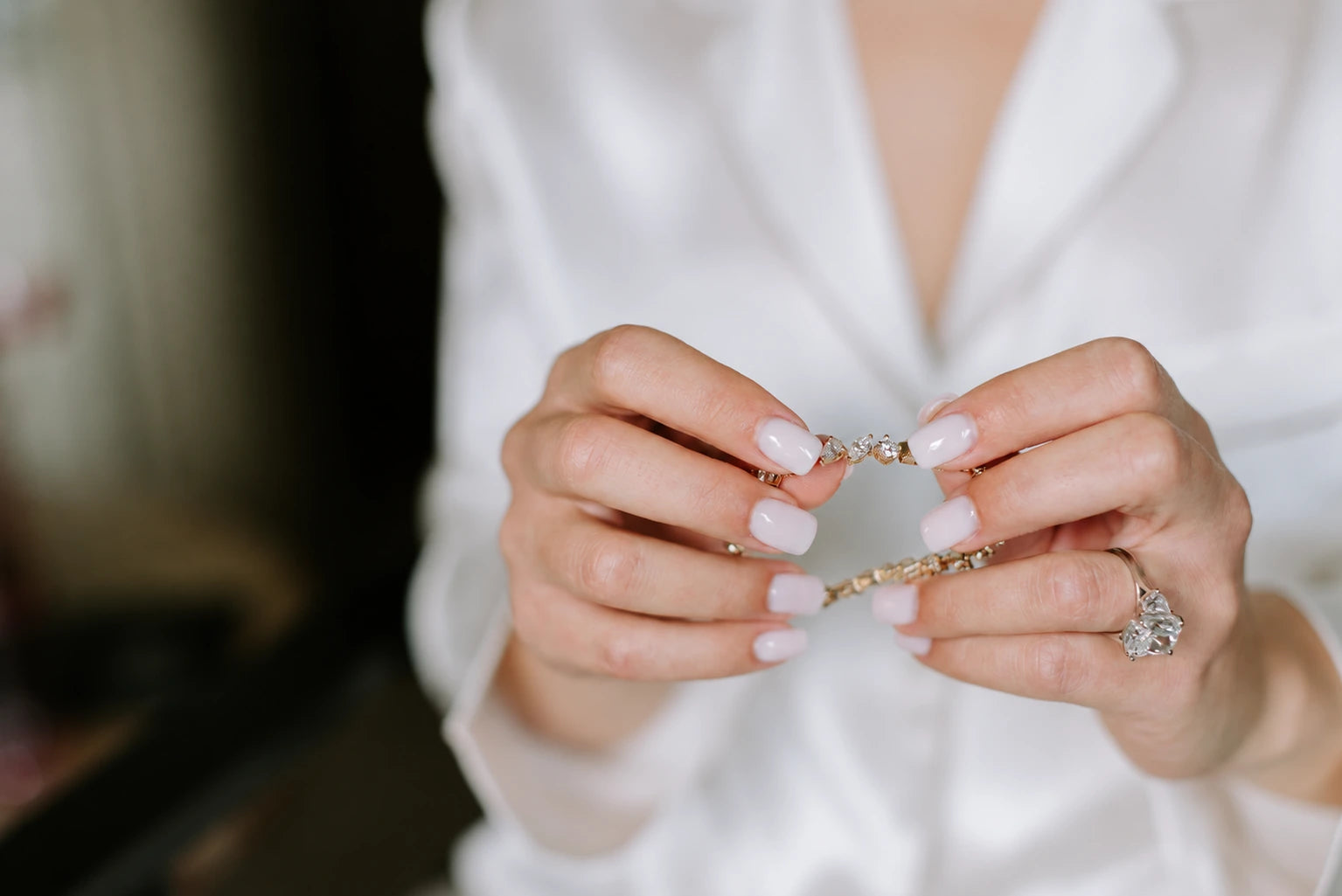 Bride in a white robe holding a diamond bracelet, wearing a diamond engagement ring