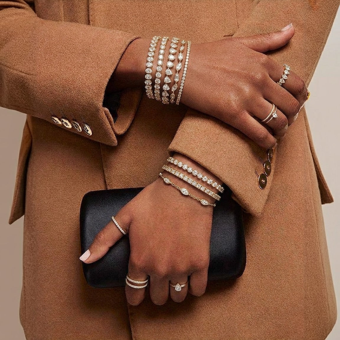 Diamond bracelets and rings worn with a tan coat