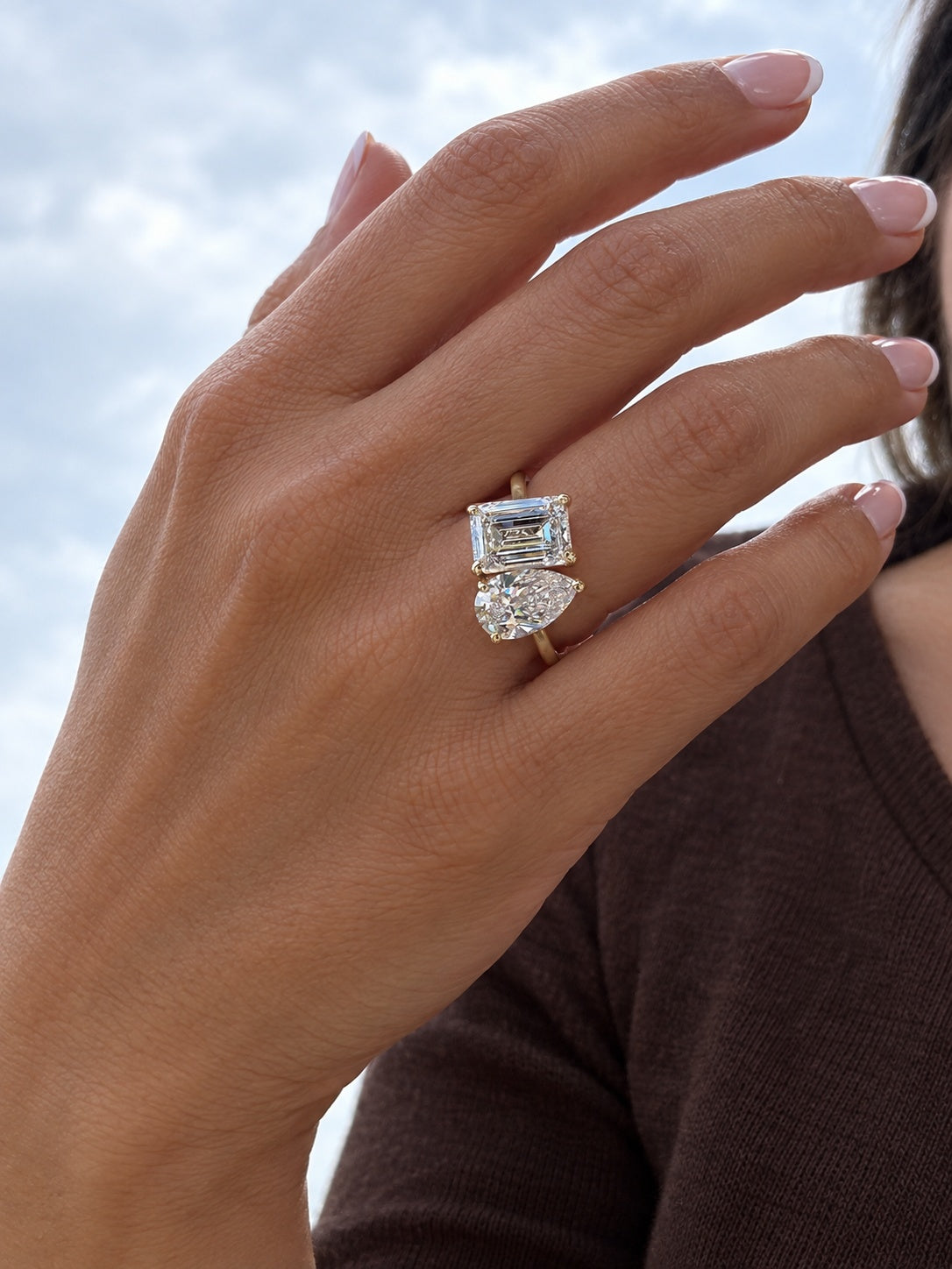 Pear and emerald-cut diamond ring worn with a French manicure and dark brown top