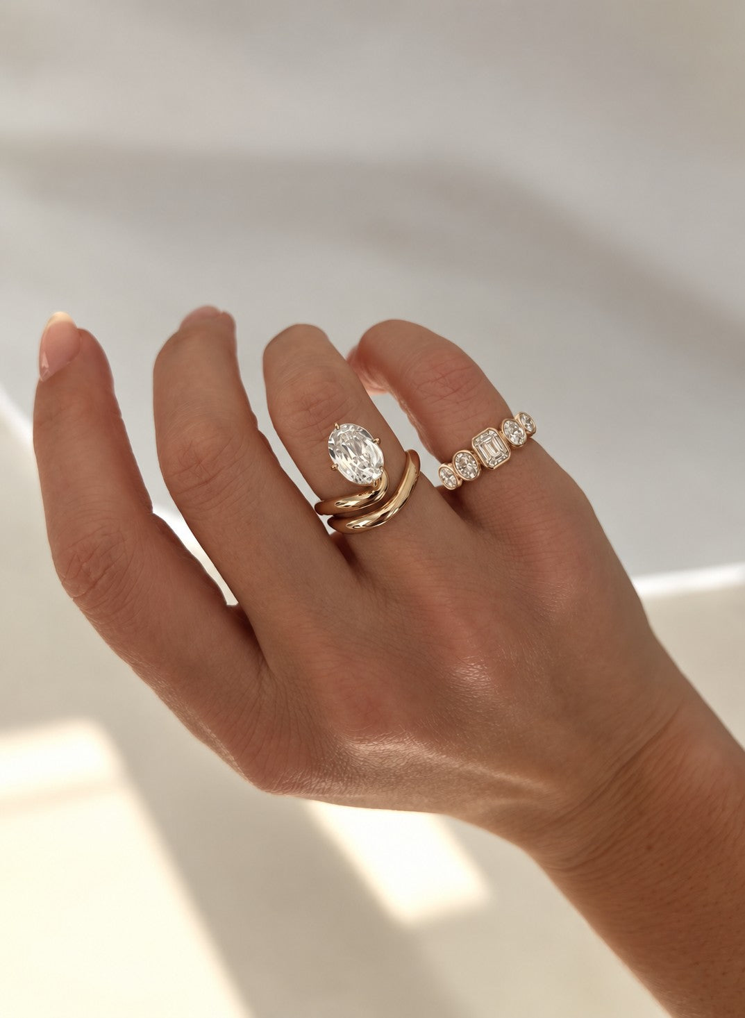 Oval diamond ring with curved gold bands beside a five-stone bezel ring